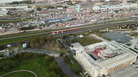 Aerial-of-a-train-passing-between-Faculty-of-Law-and-Villa-31-in-Buenos-Aires,-Argentina