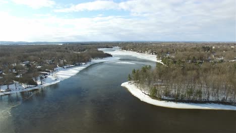 Aerial-over-icy-river-in-winter-snow-on-forested-riverbanks