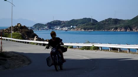 Young-man-drives-motorcycle-near-Binh-Hung-island-with-fisheries,-fishing-farms-and-fishing-nets-behind