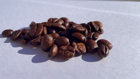 Macro-shot-of-many-roasted-coffee-beans-lighting-during-sunlight-outdoors-on-white-surface