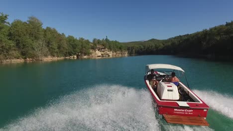 Following-red-master-craft-ski-speedboat-low-across-bright-blue-lake-lagoon-speeding-drone-shot