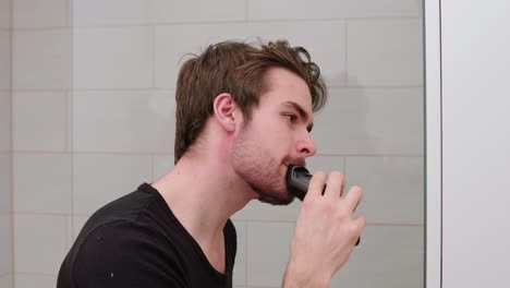 young-adult-man-trimming-and-shaving-his-beard-in-front-of-mirror-in-bathroom