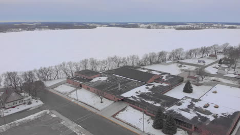 Drone-aerial-shot-over-a-frozen-lake-and-small-midwest-town-in-the-winter-to-a-school