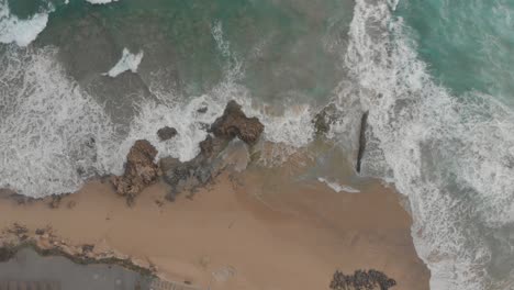 Top-down-static-shot-over-ocean-waves-crashing-on-Ponta-da-Calheta-beach,-Madeira