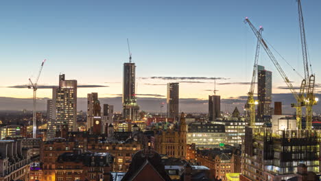 Sunset-golden-hour-time-lapse-view-of-Manchester,-UK-skyline-with-several-cranes-working-construction-of-high-rise-buildings-on-the-horizon