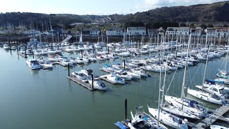 Luxury-yachts-and-sailboats-moored-in-Conwy-marina-mountain-waterfront-aerial-rising-view-North-Wales