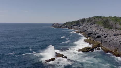 Drone-flyine-low-along-the-water-as-a-big-wave-crashes-on-the-rocky-coastline-in-Maine