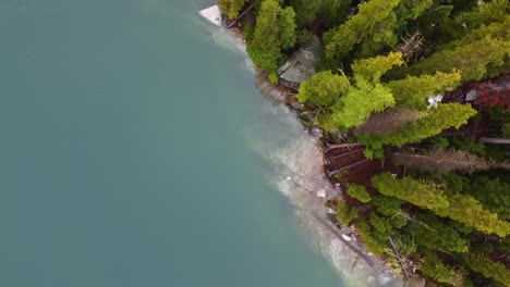 Drone-footage-of-Colchuck-Lake-and-two-drone-operators-on-rock-near-The-Enchantments-in-Washington's-Cascade-Mountain-Range---Moss-and-Tress-grow-on-the-cliffside