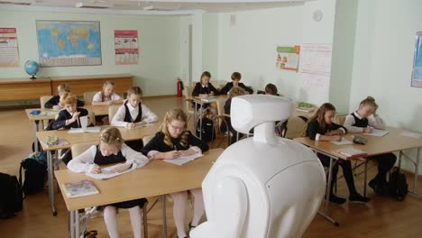 Maestro-Robot-Escuela-Futurista-Contando-Algo-Amplio-Plano-De-Un-Salón-De-Clases-Lleno-De-Estudiantes-Haciendo-Su-Tarea-O-Tarea