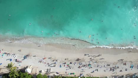 A-drone-starts-with-a-beautiful-view-of-crystal-clear-blue-waters,-sun,-sand-and-families-enjoying-their-travel-vacation-destinations-and-raises-up-to-reveal-even-more-of-the-beautiful-environment
