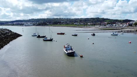 Aerial-view-moored-boats-on-Welsh-low-tide-seaside-breakwater-harbour-coastline-slow-flight-passing-boats