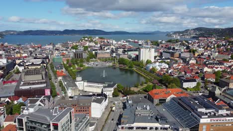 Forward-moving-aerial-Bergen-city-centre-with-water-fountain-in-park-and-seafront-in-the-background---Norway