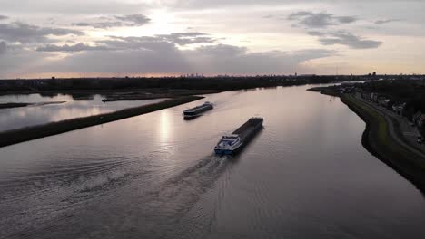 Ein-Leeres-Lastkahnschiff-Fährt-Bei-Sonnenuntergang-An-Einem-Tanker-Vorbei,-Der-Auf-Einer-Binnenwasserstraße-Fährt