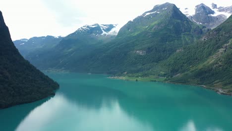 Wide-panoramic-view-over-stunning-Oldedalen-valley-with-glaciers-on-mountaintops-and-emerald-green-freshwater-lake---Sideways-moving-aerial-in-the-middle-of-glacial-lake-Olden---Norway
