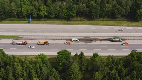Construction-area-at-a-german-autobahn-with-a-group-of-street-workers-doing-their-job-by-checking-the-intermediate-barrier-standing-next-to-their-lorries-while-cars-passing-by-the-maintenance-site