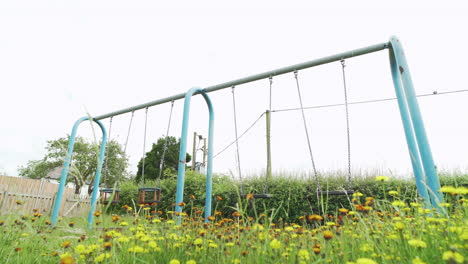 Empty-swings-in-abandoned-children's-playground-with-overgrown-grass-during-covid-19-pandemic