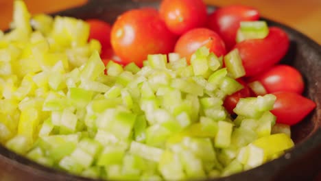 Extreme-close-up-handheld-shot-capturing-freshly-diced-green-bell-pepper-and-organic-cherry-tomato-in-mini-cast-iron-pan