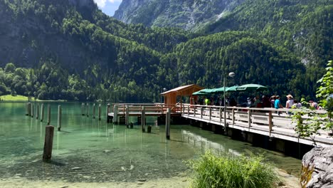 Panning-shot-of-tourists-waiting-on-wooden-jetty-port-of-electric-boat-for-cruise-on-KÃ¶nigssee-in-Germany---Beautiful-mountain-landscape-in-summer