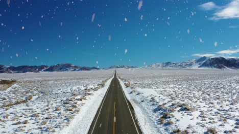 Iconic-American-country-road-in-winter-season-during-snowfall,-aerial-fly-forward-view