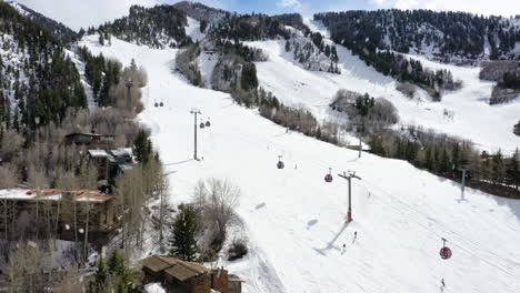 Cable-cart-lift-in-snow-resort-doing-snowfall-while-people-skiing-down-slope,-aerial-view