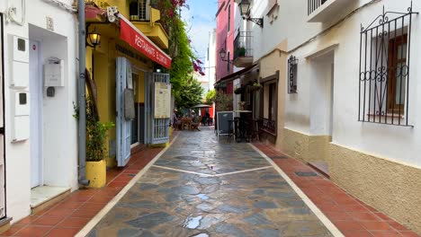 Typical-Spanish-street-in-old-city-Marbella-with-white-houses,-flowers,-balconies,-shops,-stores-and-restaurants