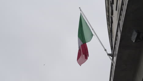 Bandera-Nacional-De-Italia-Ondeando-Mientras-Cuelga-En-La-Fachada-Del-Edificio,-Toma-En-Cámara-Lenta