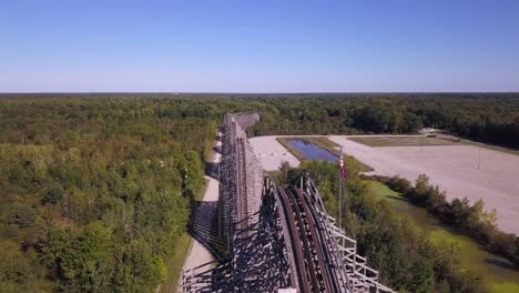 Panning-aerial-of-rollercoaster-with-American-flag-by-forest,-Michigan