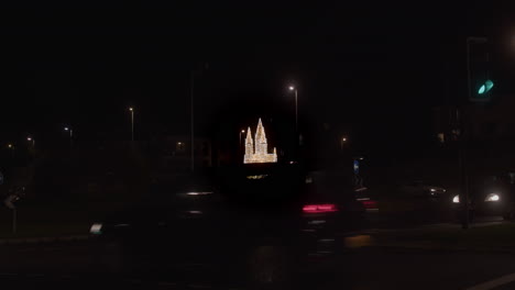 Cars-Driving-In-The-Street-At-Night-With-Cathedral-shaped-Made-From-Christmas-Lights-In-The-Distance-In-Truro,-Cornwall,-UK