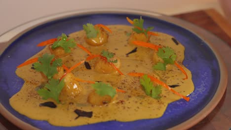 A-complete-dish-of-yellow-curry-seafood-scallop-dish,-beautifully-garnished-with-julienne-red-bell-pepper-and-parsley-spinning-on-lazy-susan-turntable