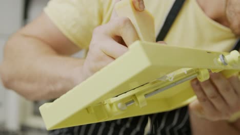Chef-slices-cheese-using-mandoline-slicer,-holding-it-in-his-hands
