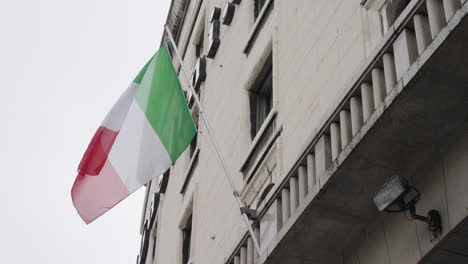 National-flag-of-Italy-waving-in-slow-motion-on-building-facade,-handheld-view