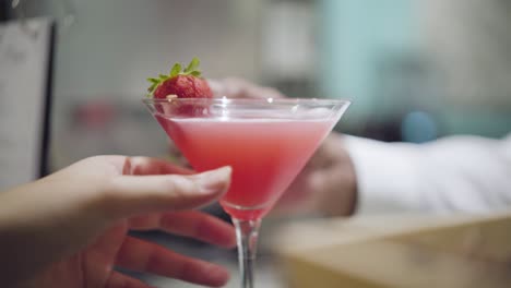 Colorful-Cocktail-with-a-strawberry-garnish,-Bartender-hands-a-drink-to-a-beautiful-lady