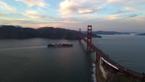 Aerial-view-of-a-cargo-ferry-driving-under-the-Golden-gate-bridge,-evening-in-San-Francisco,-USA---descending,-drone-shot