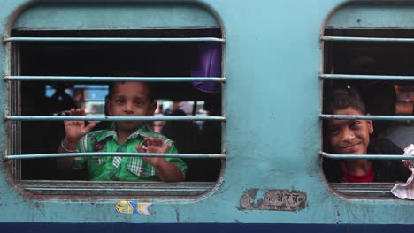Children-smiling-and-saying-hello-with-hands-on-board-of-departing-train-in-India-while-looking-at-camera