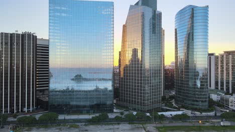 Cinematic-pull-out-shot-of-modern-business-office-buildings-with-glass-reflection,-reflecting-Puerto-Madero-harbor-on-glass-windows-during-sunset-at-downtown-Buenos-Aires-capital-city-of-Argentina