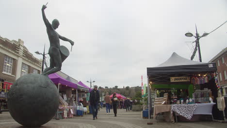 Sculptor-Tim-Shaw's-Drummer-Statue-in-the-Town-Centre-of-Truro-with-the-Farmers-Market-in-Cornwall,-England