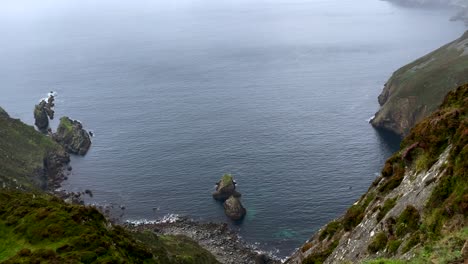 Von-Oben-Nach-Unten-Aufgenommene-Aufnahme-Idyllischer-Steiler-Grüner-Klippen-In-Irland-An-Einem-Nebligen-Und-Regnerischen-Tag---Schwenkaufnahme-Des-Ruhigen-Blauen-Atlantiks-Und-Der-Küste---4k