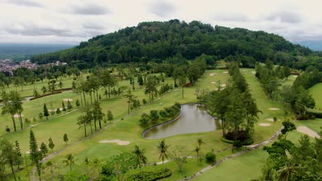 Tropical-vibrant-golf-course-near-foothills-of-Tidar-in-Magelang,-Indonesia,-aerial-view