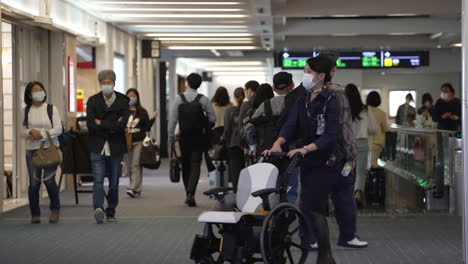 Flight-Stewardess-In-Mask-Pushing-An-Empty-Wheelchair-At-The-Airport-In-Tokyo,-Japan