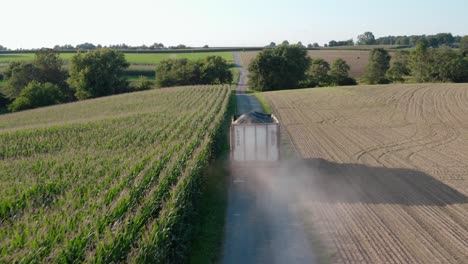 Aerial-tracking-shot-of-truck-on-dusty-farm-lane,-loaded-with-animal-feed,-corn-silage-covered-with-black-tarp