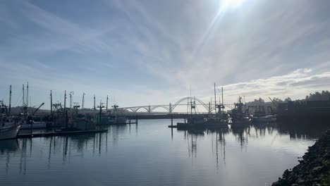 Port-Of-Newport,-Commercial-Boats-Floating-At-Calm-Bay-With-Yaquina-Bay-Bridge-In-Background-On-A-Sunny-Day