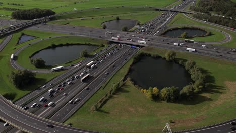 Backwards-movement-revealing-large-Oudenrijn-bypass-intersection-roundabout-near-Utrecht-with-slow-moving-vehicles-seen-from-above-with-ominous-dark-cumulus-clouds-hanging-over-it