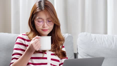 Young-woman-enjoying-a-cup-of-tea-while-using-notebook-to-chat-with-friends