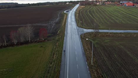 Man-Skiing-Down-Long-Isolated-Wet-Countryside-Road-Near-Ostersund,-Sweden