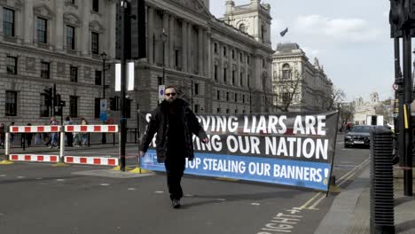 Men-In-Suits-Walk-Past-Self-Serving-Liars-Tory-Government-Banner-On-Closed-Parliament-Street-Road-On-17-March-2022