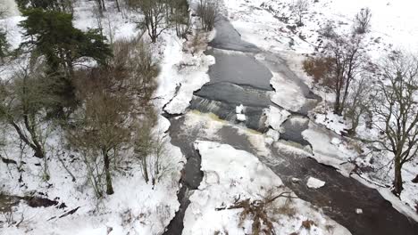 Aerial-drone-view-of-a-small-stream-in-the-winter-with-snow-all-around