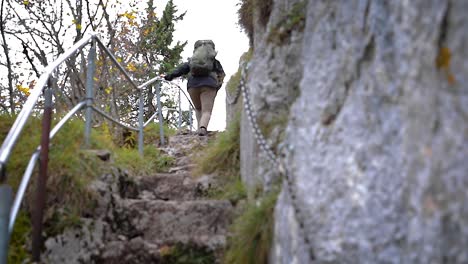 Slow-motion,-backpacker-hiking-up-stone-rock-steps-holding-handrail