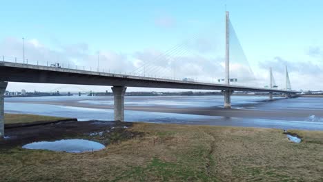 Mersey-gateway-landmark-toll-bridge-at-low-tide-with-river-marshland-aerial-view-low-orbit-left