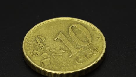 Golden-ten-cents-coin-rotating-on-a-black-surface,-macro-shot-in-4k-extreme-detail-close-up-view