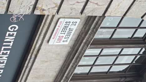 Vertical-Video-Slow-motion-revealing-shot-St-James's-Street-SW1,-street-sign-on-Old-marble-building-with-wooden-windows